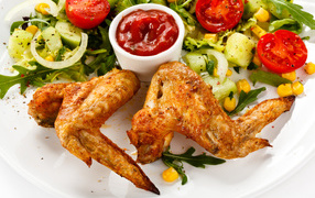 Жареные куриные крылышки с овощами и кетчупом на белой тарелке
