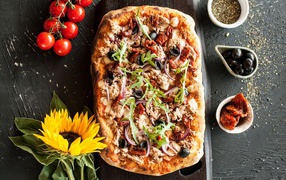 Fried pizza with meat on a table with a yellow flower of a sunflower