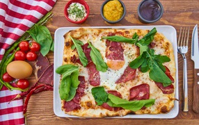 Pizza with bacon and green basil leaves on a table