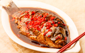Fried fish with sauce and red pepper in a white dish