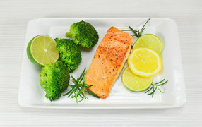 Red fish on a white plate with lemons and broccoli
