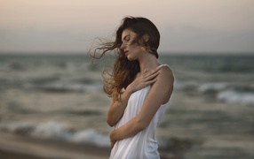 Мечтательная девушка в белом наряде стоит на берегу океана