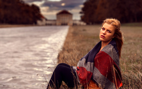 A girl in a plaid sits on the river bank