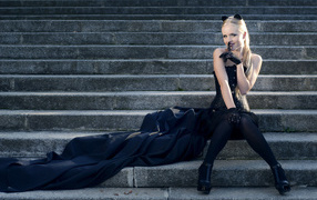 Красивая девушка блондинка  сидит на ступеньках в черном костюме