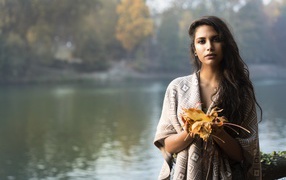 Beautiful brunette by the river with yellow leaves in hands