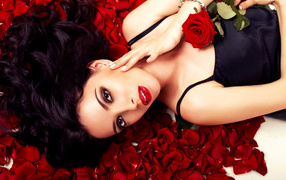 Beautiful brunette girl with a red rose lies on the petals