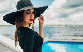 Красивая девушка в большой черной шляпе у бассейна