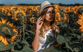Красивая девушка в шляпе стоит на поле с подсолнухами