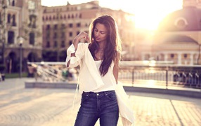 Красивая девушка в синих джинсах стоит на фоне солнца