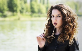 Красивая девушка с волнистыми волосами с очками в руках 