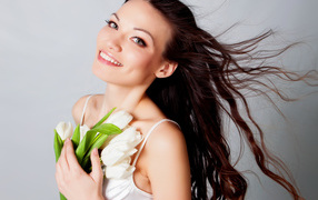 Красивая улыбающаяся брюнетка с букетом тюльпанов на сером фоне