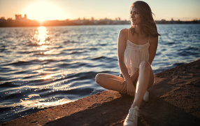 Красивая улыбающаяся девушка сидит в лучах солнца у реки