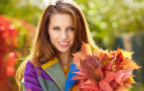 Красивая улыбающаяся девушка с букетом желтых листьев в руке