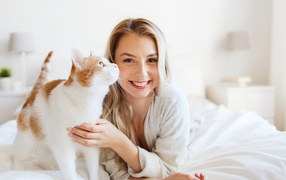 Красивая улыбающаяся девушка с котом лежит на кровати