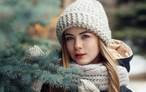Beautiful young blue-eyed girl at a spruce branch in winter