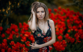 Beautiful young girl posing on a background of red tulips