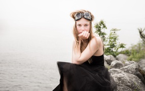 Девушка блондинка с очками на голове сидит на камне