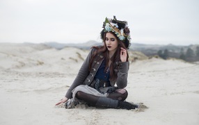 Девушка брюнетка  в костюме сидит на песке 