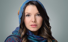 Face of a young brown-eyed girl in a scarf on a gray background