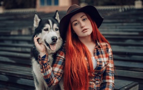 Red-haired girl in black hat sits with Husky