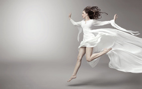 Running beautiful girl in white dress on gray background