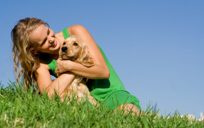 Улыбающаяся девушка со щенком на зеленой траве