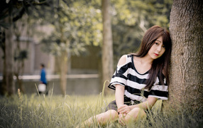 Молодая девушка азиатка сидит на траве у дерева