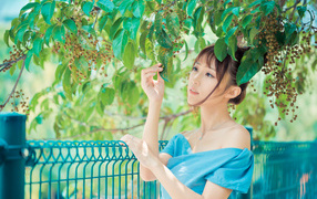 Молодая красивая девушка азиатка стоит у ветки с зелеными листьями