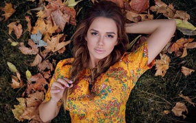 Young brunette lies on grass with dry leaves