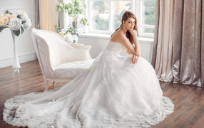 Молодая девушка в красивом свадебном платье сидит в белом кресле