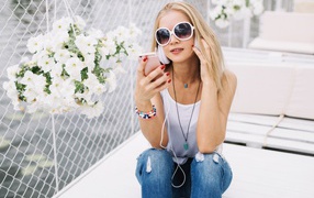 Молодая девушка в солнечных очках сидит с телефоном у белых цветов