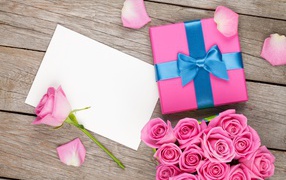 Коробка с подарком на столе с букетом розовых роз и листом бумаги