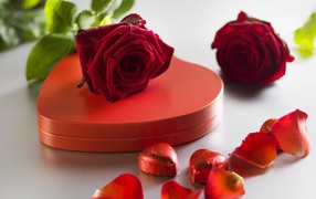 Large red box in the shape of heart with chocolate sweets and red roses