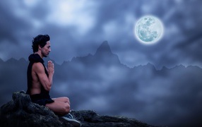 Мужчина медитирует на камне ночью в полнолуние