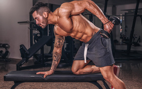 Мускулистый мужчина занимается в спортзале с гантелей