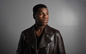 Актер  Джон Бойега в кожаной куртке на сером фоне