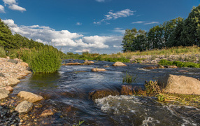 Быстрая речная вода стекает по камням под красивым голубым небом