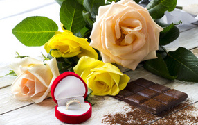Букет роз на столе с шоколадкой и красной коробочкой с обручальным кольцом