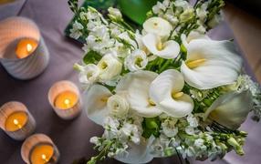 Букет белых цветов зантедеския и левкой с зажженными свечами на столе