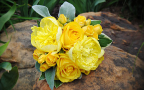 A bouquet of yellow roses with yellow peonies lies on a rock