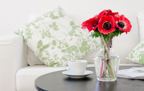 Букет красных цветов анемоны в вазе на столе с белой чашкой