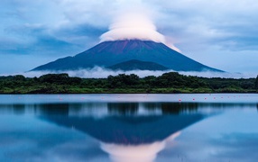 Вулкан Фудзияма в белых облаках отражается в воде озера