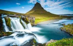 Водопад стекает в реку на фоне горы под красивым небом