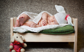 A baby boy is sleeping in a wooden bed in a white knitted bunny costume