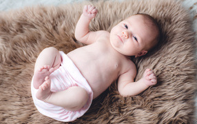 Грудной ребенок лежит на меховом покрывале