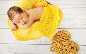 Грудной ребенок спит на желтой подушке с плетеным сердцем