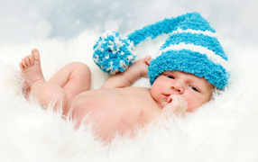 Грудной ребенок в голубой шапке с бубоном на голове