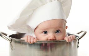 A baby child in a chef's hat sits in a large saucepan