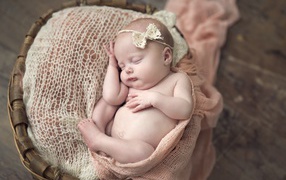 A baby with a bow on his head sleeps in a basket