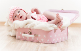 A cute baby lies in a pink suitcase